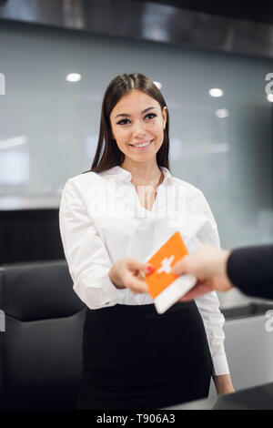 Friendly woman staff taking passport from passenger at airport check in desk Stock Photo