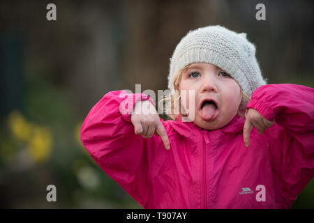 Little girl in hat pulling faces in garden Stock Photo