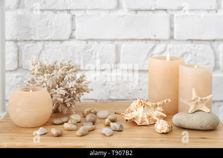 Seashells, pebbles and burning candles on table near white brick wall Stock Photo