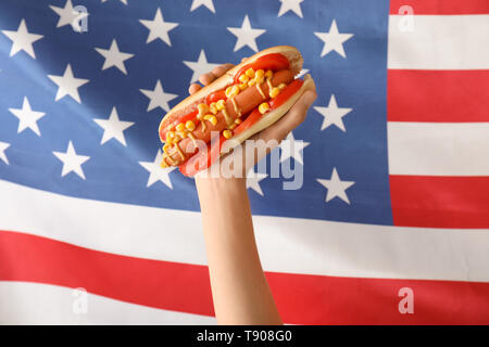 Woman holding tasty hot dog against USA flag Stock Photo