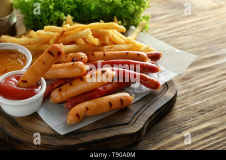 Delicious grilled sausages with sauces and french fries on wooden board Stock Photo