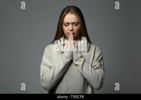 Beautiful young woman praying on grey background Stock Photo