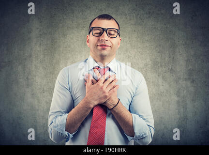 Business man with eyes closed keeps hands on chest near heart, shows kindness, expresses sincere emotions, being kind hearted. Body language feelings  Stock Photo