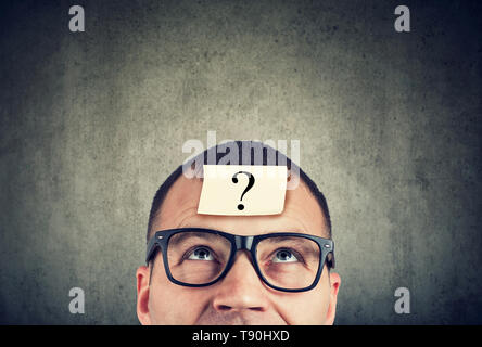 thinking man in glasses with question mark looking up on gray wall background Stock Photo