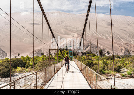 Man riding a bike on the footbridge over Acari River and Cerro Toro Mata in the background. Acari, Department of Arequipa, Peru. Stock Photo