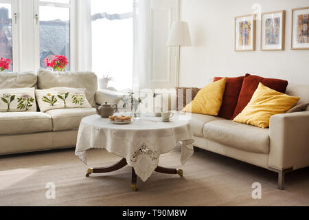 Sunlit classic style living room with two leather sofas and tea served on a small round table Stock Photo