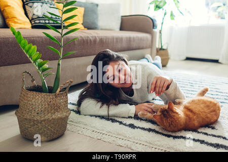 Young woman playing with cat on carpet at home. Master lying on floor with her pet Stock Photo