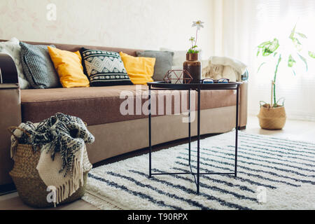 Flat interior of living room decorated with baskets, plants and carpet. Couch with cushions and table Stock Photo