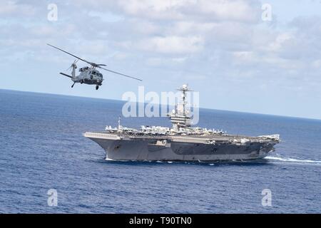 A U.S. Navy MH-60S Sea Hawk helicopter flies alongside the Nimitz-class aircraft carrier USS John C. Stennis during routine patrol May 9, 2019 underway in the Atlantic Ocean. Stock Photo