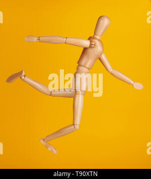 Wooden doll in kick ball pose side view isolated on yellow background Stock Photo