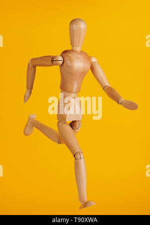 Running wooden doll isolated on yellow background Stock Photo