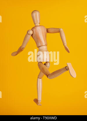 Wooden man toy running back view isolated on yellow background Stock Photo