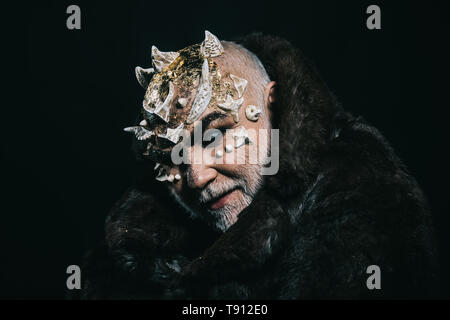 Alien, demon, sorcerer makeup. Horror and fantasy concept. Man with thorns or warts in fur coat. Demon on black background, copy space. Senior man Stock Photo