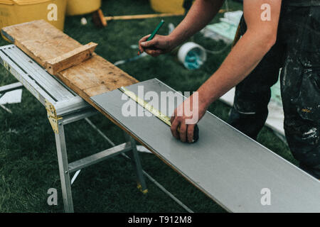 Builder working, measuring and cutting boards for house renovation and upkeep. Shows tools and equipment being used with materials in the background Stock Photo