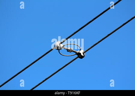 Two power line utility black electrical wires held together with strong insulators and spacers on clear blue sky background Stock Photo