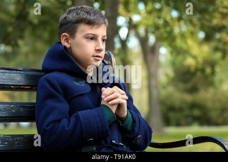 Praying little boy sitting on bench in park Stock Photo