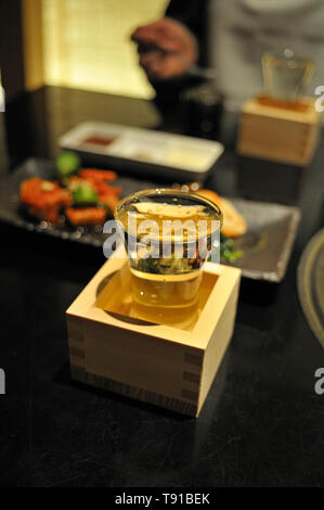 Full sake cup in a wooden box on a table in a restaurant in Tokyo Stock Photo