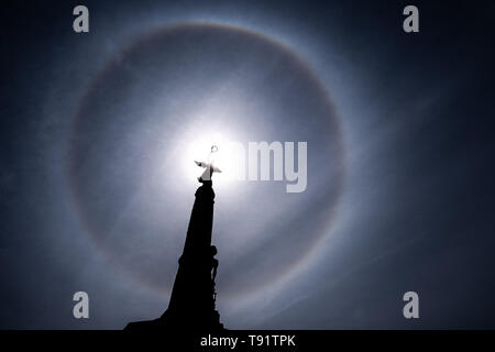 Aberystwyth Wales UK, Thursday 16 May 2019  UK Weather: A perfect circular sun halo , formed as the rays of the sun shine through ice crystals in the upper atmosphere, seen in the sky above the silhouette of the war memorial Aberystwyth. The halos, always at 22º from the sun,  often  indicate that rain will fall within the next 24 hours, since the cirrostratus clouds that cause them can signify an approaching frontal system. The  weather is set to change overnight from the fine warm conditions to cooler and wetter days, more typical of mid May.  photo credit Keith Morris / Alamy Live News Stock Photo