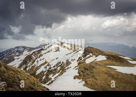 Dramatic, moody view from Midzor summit, the highest peak of old mountain, during transition period between winter and spring with remaining snow Stock Photo