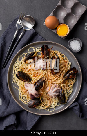Close up tasty pasta with octopus and mussels on dark background, fork, knife and napkin near. Concept of romantic dinner. Macro, Flat lay, table top Stock Photo
