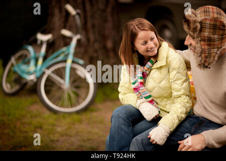 Young couple wearing warm clothes look at each other while sitting in a yard. Stock Photo