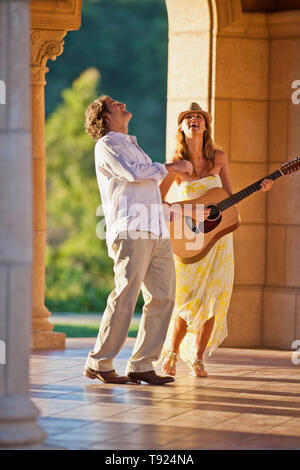 Smiling mid adult woman playing an acoustic guitar while her partner looks on. Stock Photo