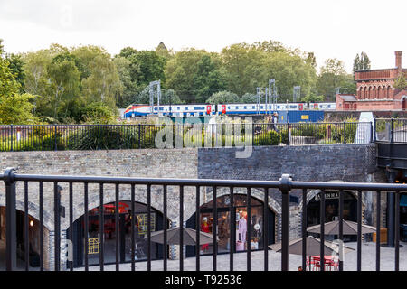 View across the recently completed Coal Drops Yard and Regent's Canal to a train approaching St Pancras Station, a Victorian water tower on the right Stock Photo