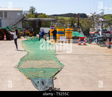 young woman takes a selfie on her mobile phone while fishermen mend a large trawler fishing net Stock Photo