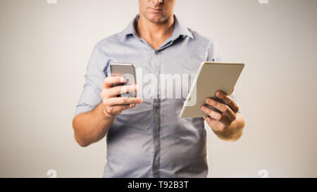 Man dressed casually in collared shirt using a tablet and phone -  Casual business concept image with copy space for text. Stock Photo