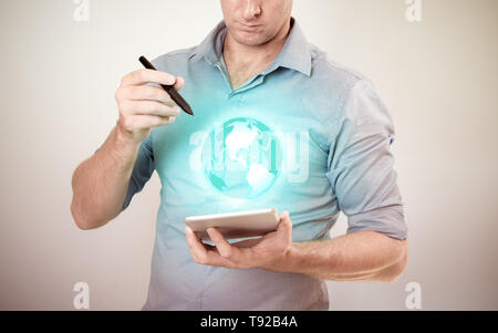 Casually dressed business man  holding tablet with pen looking at projected virtual globe on plain background. Stock Photo