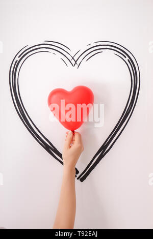 Female hand holding heart-shaped air balloon near white wall Stock Photo