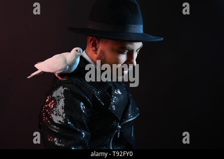 Male magician with white pigeon on dark background Stock Photo