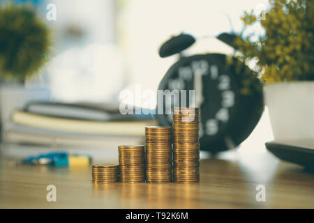 Coin stack and financial graph paper sheet with notebook calculator and alarm clock on working table, business finance concept idea. Stock Photo