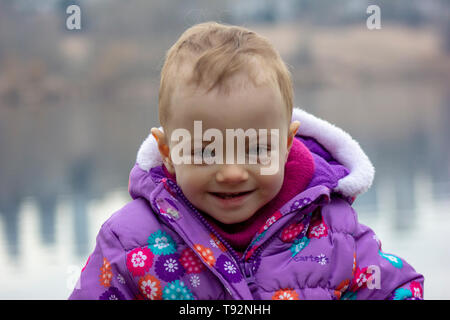 20 months old baby is enjoying the nice Winter weather. Bundled up for the cold. 1.5 years old toddler walking in parks when the sun is out. Stock Photo