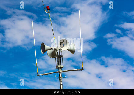 A group of loudspeakers warning about the danger on a metal pillar against a blue sky background. Stock Photo