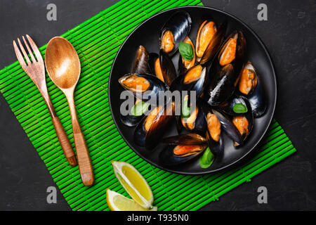 Seafood mussels and basil leaves in a black plate on bamboo mat and stone table. Top view. Stock Photo