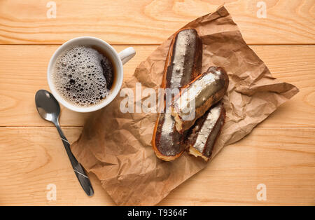Delicious eclairs and cup of coffee on wooden table, top view Stock Photo