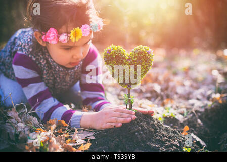 Beautiful little girl planting a heart-shaped tree and dreaming of a beautiful future Stock Photo