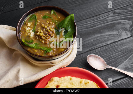 Mung Dhal with green spinach at black wooden tabletop. Moong Dal -  Indian Cuisine curry. Vegetarian dish with chapati. Copy Space Stock Photo