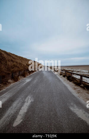 Long dark grey asphalt road between grassy hill and scenic beach next to baltic sea shoreline in summer Stock Photo