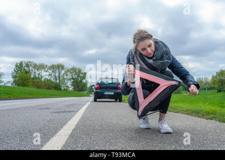 A woman is trying to build her warning triangle behind her car Stock Photo