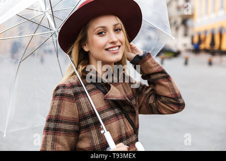 Beautiful young stylish blonde woman wearing a coat walking outdoors, holding umbrella Stock Photo