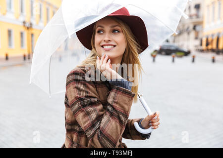 Beautiful young stylish blonde woman wearing a coat walking outdoors, holding umbrella Stock Photo
