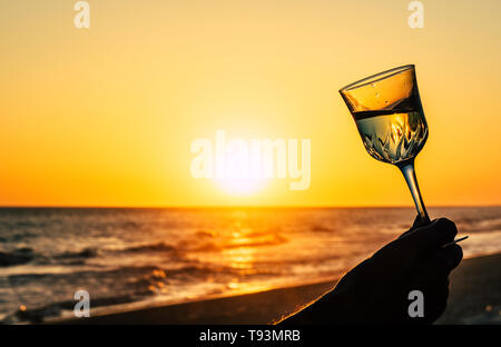 Romantic glass of wine on the beach at orange sky and sun, sunset Glasses of white wine against sunset, cup white wine with drops on the orange sky ba Stock Photo