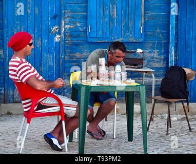 Fishermen eating in front of Blue fisher house or hut in Olhos de Agua at the Algarve coast of Portugal Stock Photo