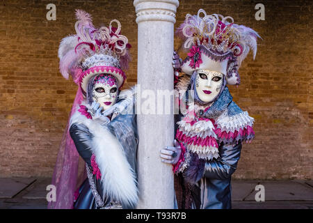 Portraits of a masked couple in beautiful creative costumes, posing in a backyard with pillars, celebrating the Venetian Carnival Stock Photo