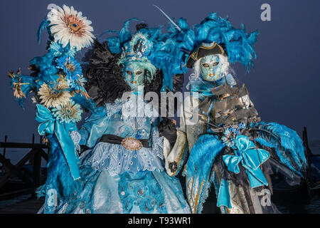 Portraits of a masked couple in beautiful creative costumes, posing at Grand Canal, Canal Grande, celebrating the Venetian Carnival Stock Photo