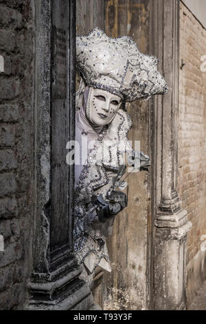 Portrait of a masculin masked person in a beautiful creative costume, posing in front of an ailing brick wall, celebrating the Venetian Carnival Stock Photo