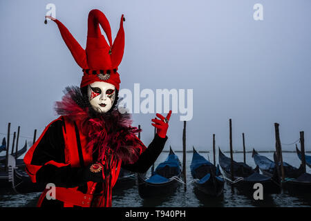 Portrait of a feminin masked person in a beautiful creative harlequin costume, posing at Grand Canal, Canal Grande, celebrating the Venetian Carnival Stock Photo