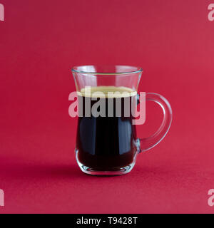 Transparent cup of black coffee placed on a red surface. Stock Photo